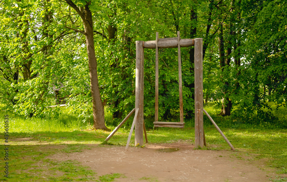 A wooden swing on a forest lawn is illuminated by the sun. A wooden swing on a forest lawn is illuminated by the sun.