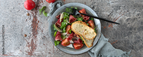 flat lay plate of salad with arugula, bresaola and tomatoes on rusty table photo