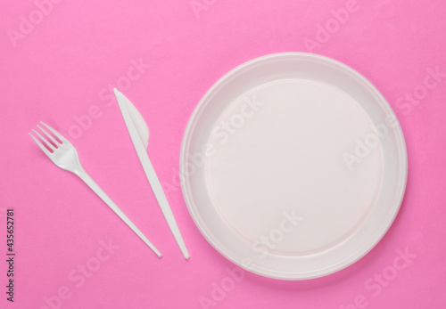 Plastic plate with fork and knife on pink background. Picnic. Plastic pollution. Top view