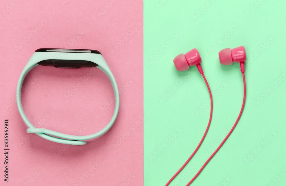 Earphones with smart bracelet on pink blue pastel background. Modern gadgets. Top view Earphones with smart bracelet on pink blue pastel background. Modern gadgets. Top view