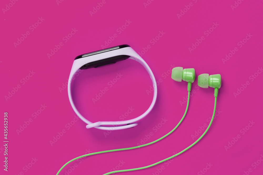 Fototapeta premium Earphones with smart bracelet on pink background. Modern gadgets. Top view