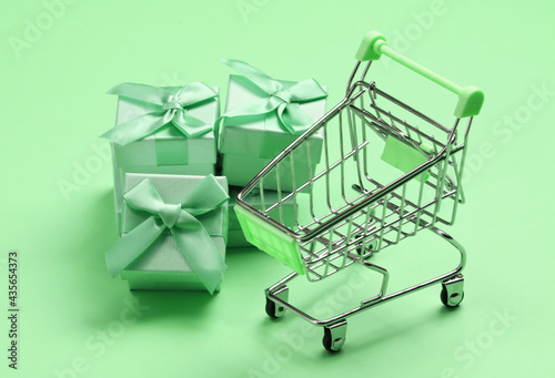 Supermarket trolley with gift boxes on green pastel background