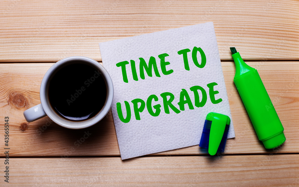 On a wooden table, a cup of coffee, a green marker and a napkin with the text TIME TO UPGRADE On a wooden table, a cup of coffee, a green marker and a napkin with the text TIME TO UPGRADE