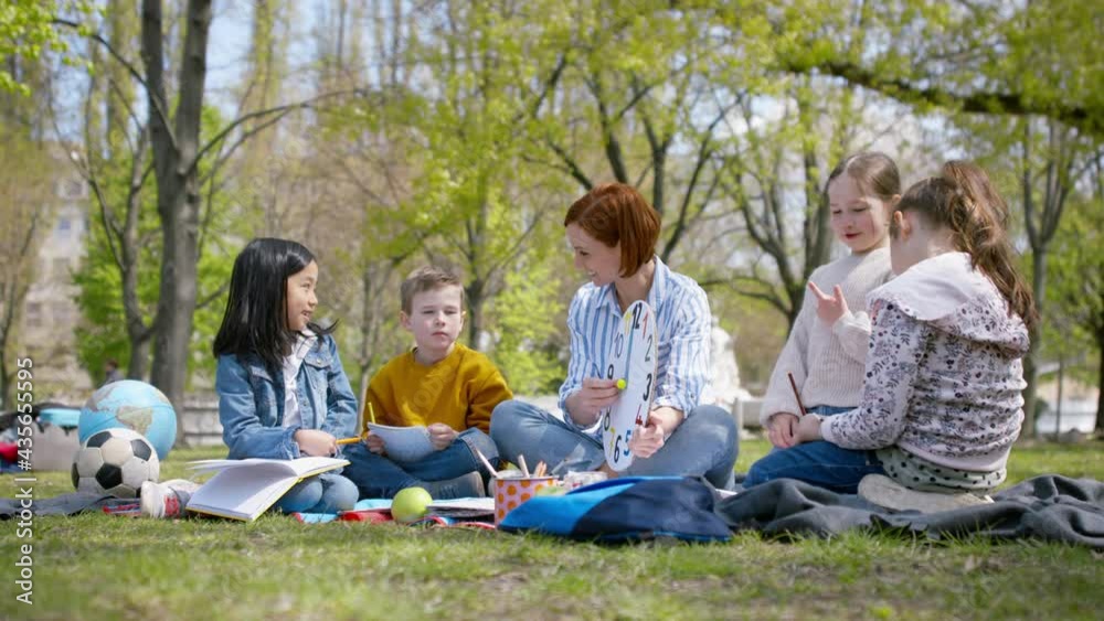 Teacher with small children sitting outdoors in city park, learning group education concept. Teacher with small children sitting outdoors in city park, learning group education concept.
