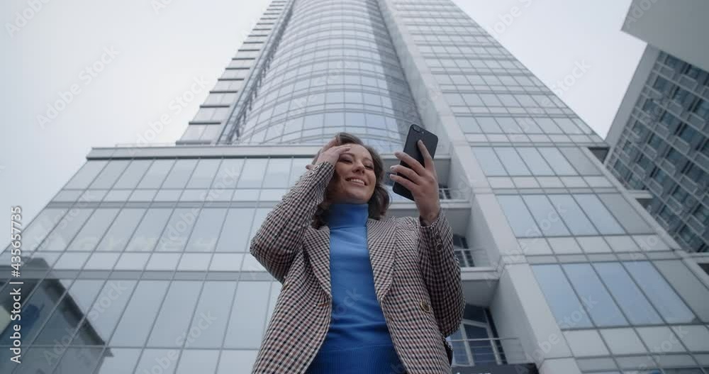 Young woman in jacket stands at the office center and gets text message in her phone, woman smiles when watch to the phone screen and get good news, city life and electronics, 4k Prores HQ Young woman in jacket stands at the office center and gets text message in her phone, woman smiles when watch to the phone screen and get good news, city life and electronics, 4k Prores HQ