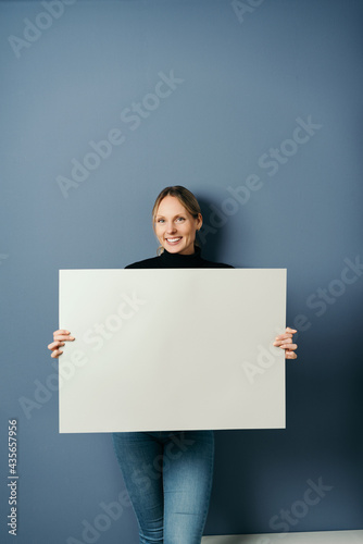 Happy friendly amiling young woman holding a blank white placard