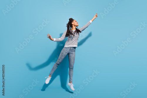 Full size photo of young black girl happy positive smile jump up catch umbrella isolated over blue color background