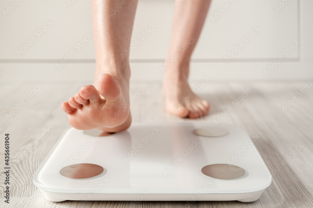 Woman foot takes a step onto a smart scale that makes bioelectric impedance  analysis, BIA, body fat measurements. Stock Photo
