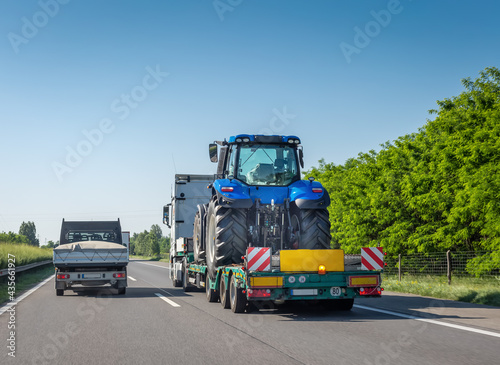 New blue tractor on long trailer platform of truck for transporting heavy machinery on highway. Transportation of agricultural machinery