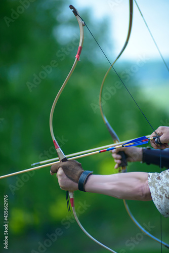 professional archers shooting with modern longbows at meadow
