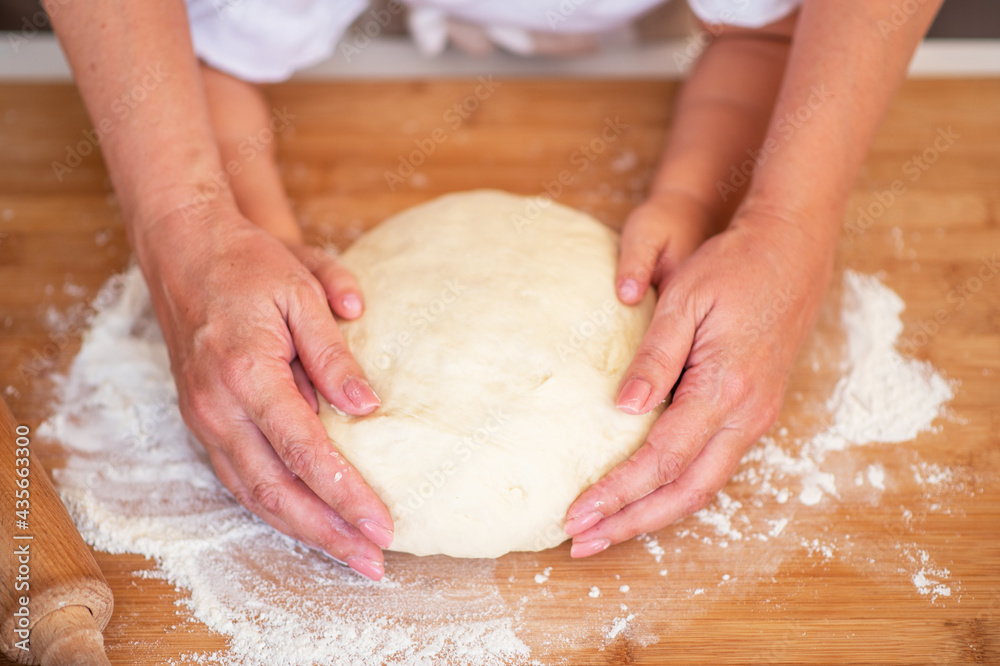 Mother and child hands prepares the dough with flour on rustic wooden table from above. Homemade pastry for bread or pizza. Bakery background. Mother and child hands prepares the dough with flour on rustic wooden table from above. Homemade pastry for bread or pizza. Bakery background.