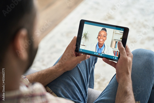 Young indian latin bearded businessman having videocall videoconference at home with black female doctor therapist using tablet computer. Online virtual telemedicine health care concept. photo
