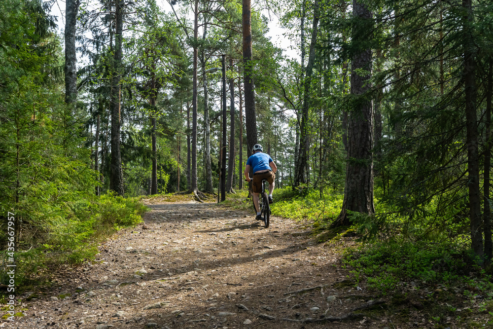 Man Cyclist on sport mountain bike on forest track. Male mountain bike racer cycling on trail with tree roots. Mountain biker rides in spring fresh air forest. Sports motivation and inspiration.