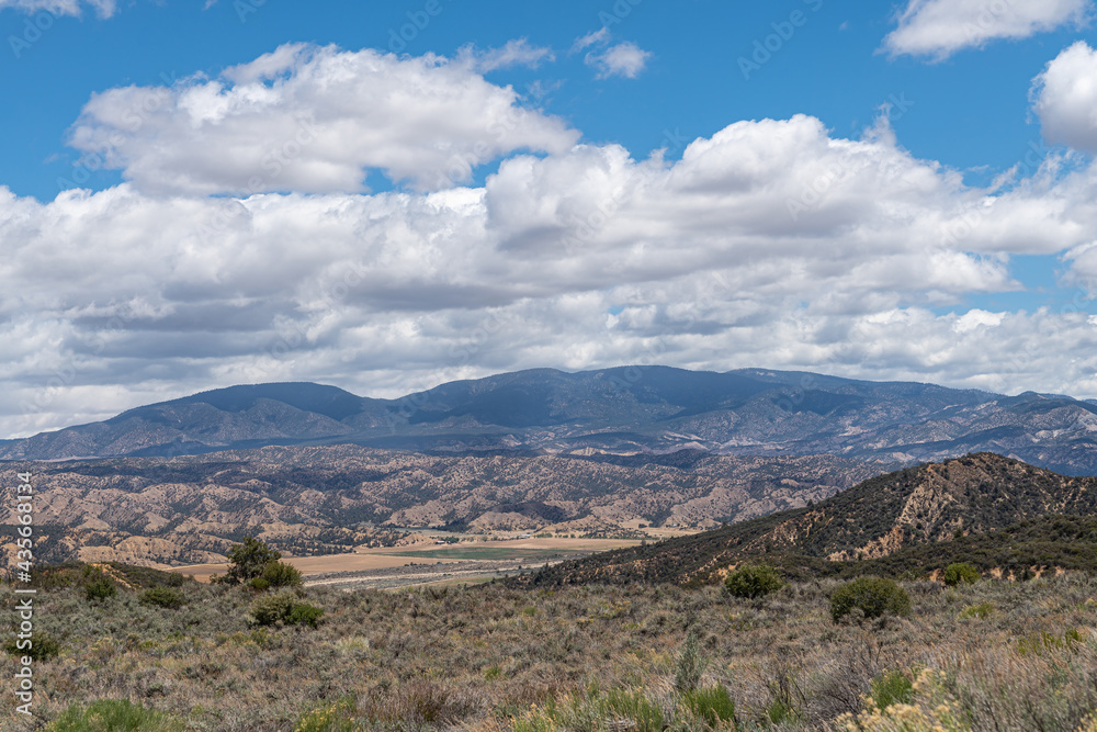 Los Padres National Forest, CA, USA - May 21, 2021: Dry mountain range in eastern part under blue cloudscape with agriculture in valley. Shrub vegetation.