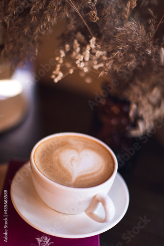 cup of cappuccino and twig of dried flowers
