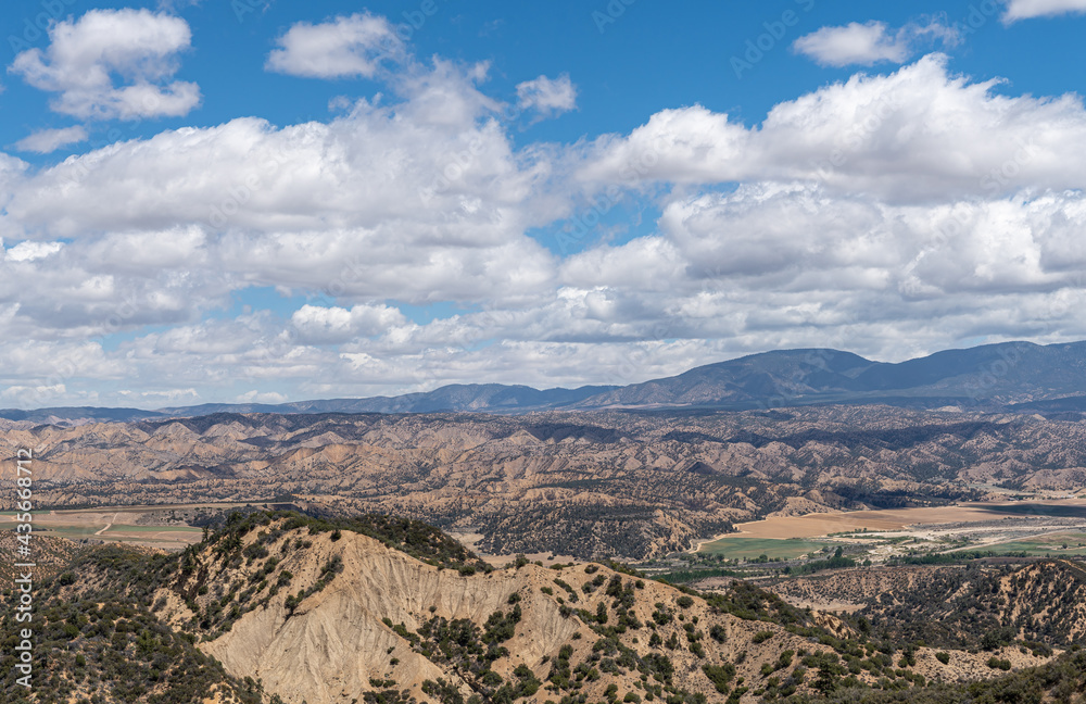 Los Padres National Forest, CA, USA - May 21, 2021: Dry mountain range in eastern part under heavy blue cloudscape with agriculture in valley. Shrub vegetation.