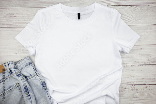 White womens cotton Tshirt mockup with blue jeans pants on wooden background. Design t shirt template, print presentation mock up. Top view flat lay. 