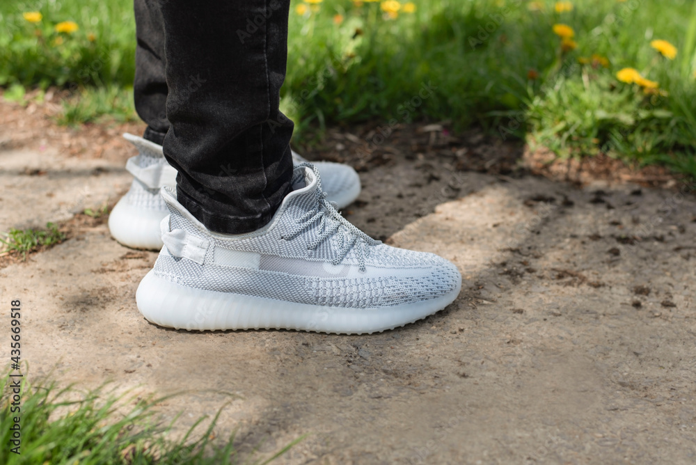 Modern light sneakers made of light fabric for comfortable walking in summer, in the warm season. Sports shoes on a background of green grass and walkway
