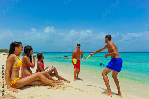 Girls and guys at the beach, girls sitting on the sand and guys playing beach paddle ball, interracial, black