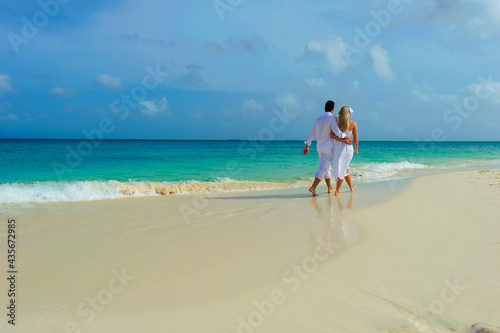 Young couple walking on the beach, in white outfits