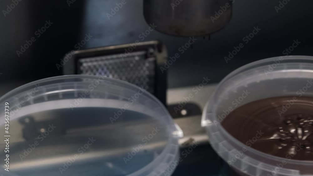 Closeup shot of pouring chocolate mixture into a plastic container. Modern working food equipment. production of chocolates. technological process. liquid chocolate mass is poured from the machine. Closeup shot of pouring chocolate mixture into a plastic container. Modern working food equipment. production of chocolates. technological process. liquid chocolate mass is poured from the machine.