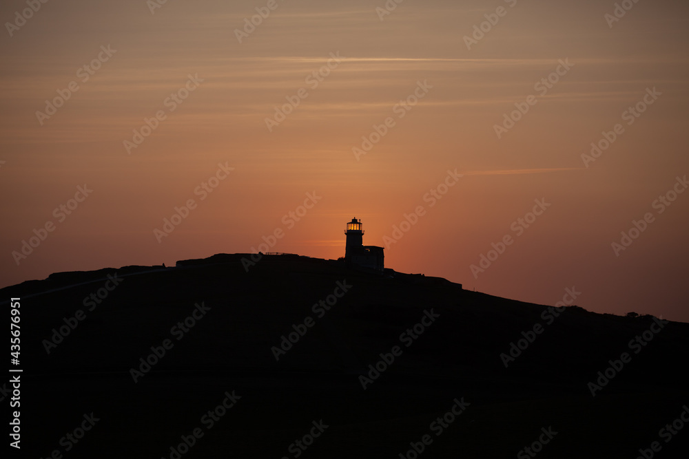 The sun sets behind a silhouetted Belle Tout ligthhouse in Sussex UK.