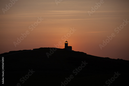 The sun sets behind a silhouetted Belle Tout ligthhouse in Sussex UK.