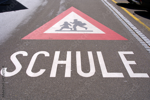Attention traffic sign watch out for school kids with text Schule (German, translation is school) painted on road near school building. Photo taken May 25th, 2021, Zurich, Switzerland. © Michael Derrer Fuchs