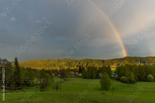 Rainbow over Bernov village in sunset evening with green meadows