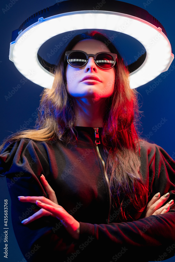 Future girl. Cyberpunk portrait. Science fiction. Galaxy portal. Red neon light futuristic female alien in sunglasses with white LED circle halo illumination isolated on dark blue. Future girl. Cyberpunk portrait. Science fiction. Galaxy portal. Red neon light futuristic female alien in sunglasses with white LED circle halo illumination isolated on dark blue.