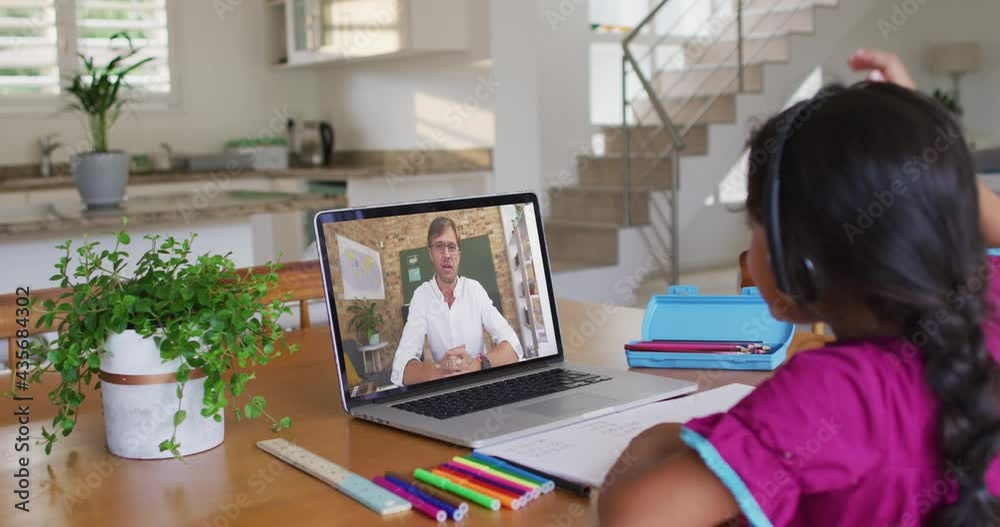 African american girl doing homework while having a video call with male teacher on laptop at home African american girl doing homework while having a video call with male teacher on laptop at home