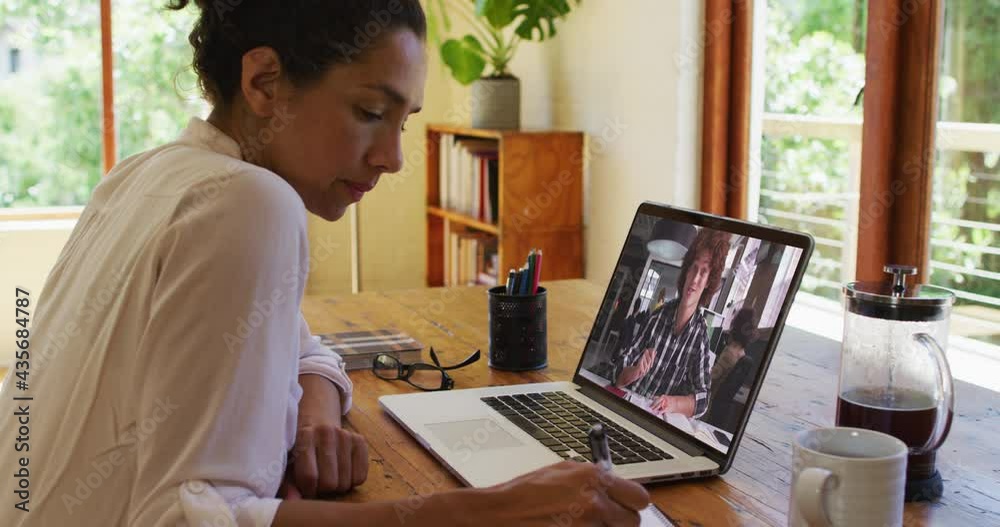 Mixed race businesswoman sitting at desk using laptop having video call with male colleague Mixed race businesswoman sitting at desk using laptop having video call with male colleague