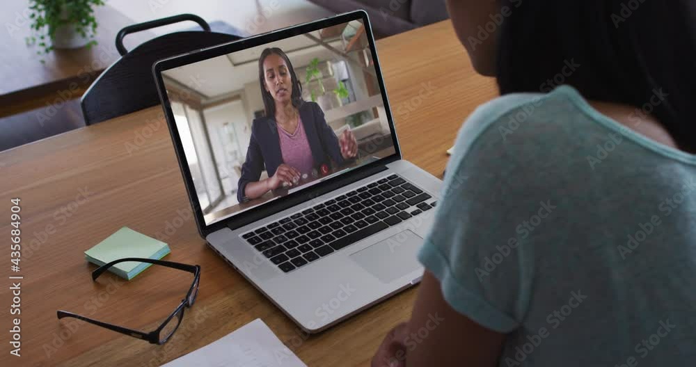Mixed race businesswoman sitting at desk using laptop having video call with female colleague Mixed race businesswoman sitting at desk using laptop having video call with female colleague
