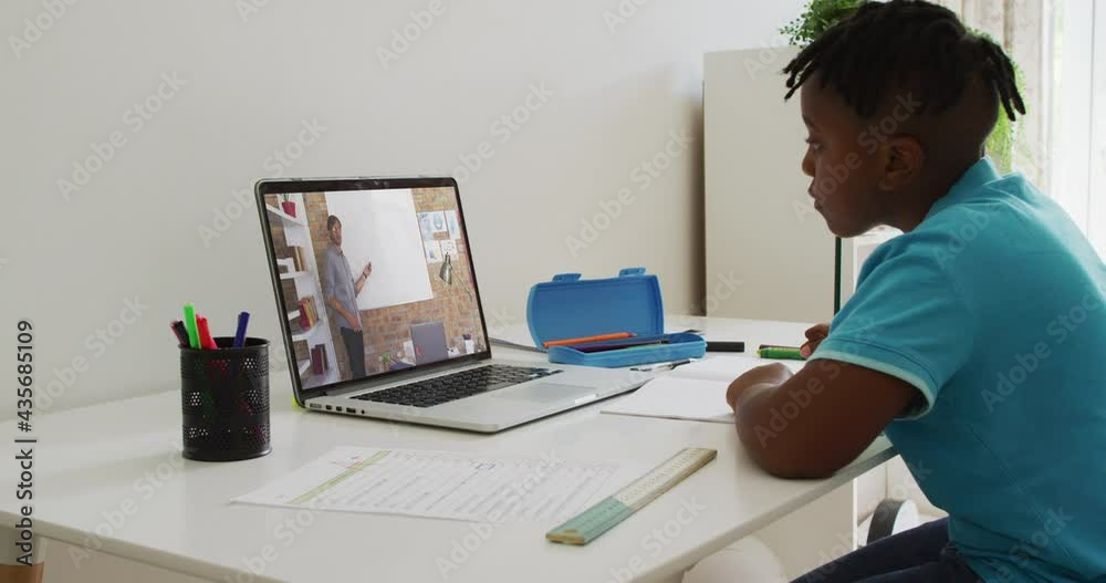 African american boy doing homework while having a video call with male teacher on laptop at home African american boy doing homework while having a video call with male teacher on laptop at home