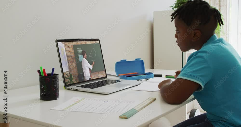 African american boy doing homework while having a video call with male teacher on laptop at home African american boy doing homework while having a video call with male teacher on laptop at home