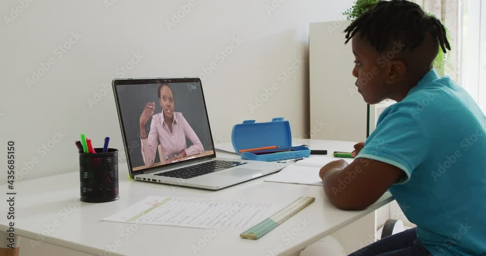 African american boy doing homework while having a video call with female teacher on laptop at home African american boy doing homework while having a video call with female teacher on laptop at home