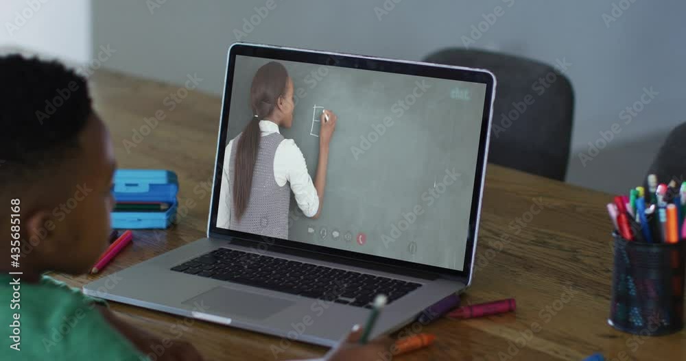 African american boy doing homework while having a video call with female teacher on laptop at home African american boy doing homework while having a video call with female teacher on laptop at home