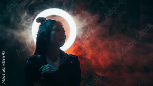 Night people banner. Cyberpunk style. Apocalyptic future. Blue neon light Asian girl in black leather jacket with white halo ring in red color steam on dark empty space background. © golubovy