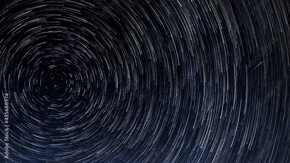 Stellar trails, the rotation of bright stars at night around the Polar Star against a blue sky and a meteor Stellar trails, the rotation of bright stars at night around the Polar Star against a blue sky and a meteor