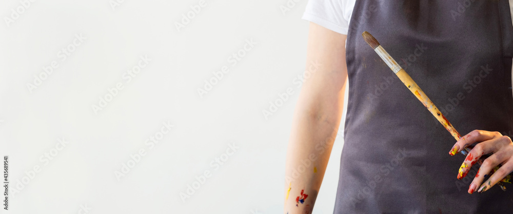 Art painting. Information banner. Artist education. Advertising background. Unrecognizable woman in apron holding professional brush in hand with colorful spots isolated white copy space.