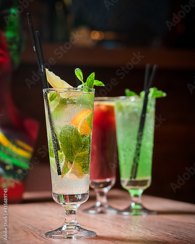 Cold lemonade sweetened lemon-flavored carbonated drink traditionally homemade served in tall drinking glass with slice of orange fruit, mint leaves and ice cubes on brown wooden table at night club