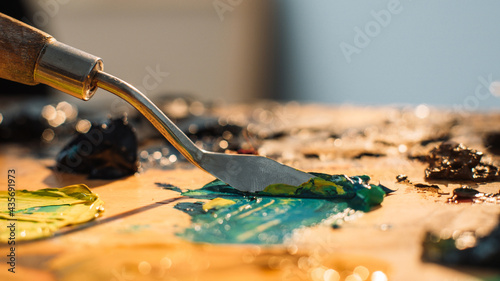 Artist work. Painting art. Professional craft. Spatula mixing blue yellow black oil or acrylic paint colors on old stained wooden palette. photo