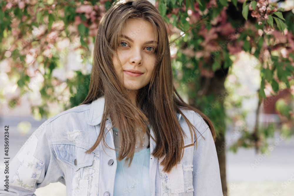 Portrait of young mixed race beauty american woman with long hair style standing on street near sakura trees, looking friendly at camera. Human face, ideal natural make up skin concept. Portrait of young mixed race beauty american woman with long hair style standing on street near sakura trees, looking friendly at camera. Human face, ideal natural make up skin concept.