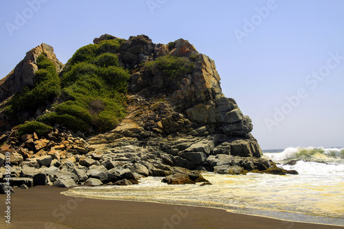 View on small bay with black volcanic lava sand, foaming waves and isolated rock with spare green vegetation - Cobquecura Piedra De La Loberia, Pacific coast, Chile photo