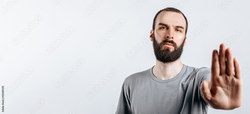 Portrait of handsome young man frowning while looking at camera holding hand opposite and saying stop gesture on white background with space for advertisement mock up Portrait of handsome young man frowning while looking at camera holding hand opposite and saying stop gesture on white background with space for advertisement mock up