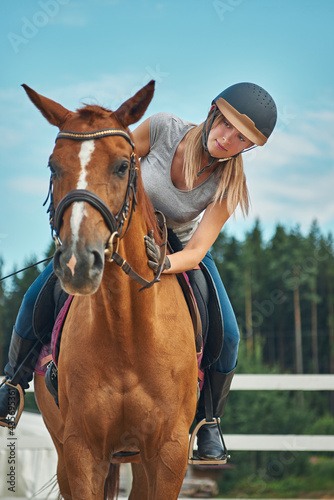 girl rider in helmet stroking horse sitting astride