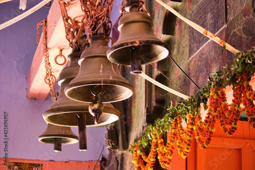 Selective focus close up of three temple bells hanging at the entrance of a hindu temple and yellow flowers on door. photo