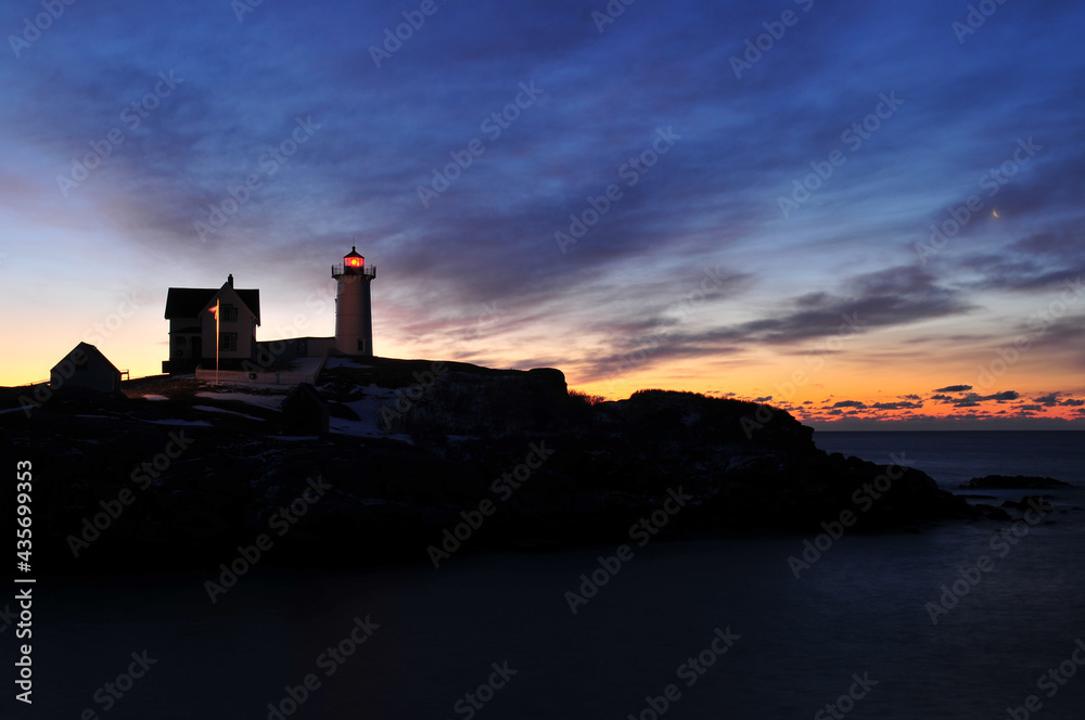 Moonset and the beginning of a winter sunrise over the Nubble Lighthouse on the coast of Maine