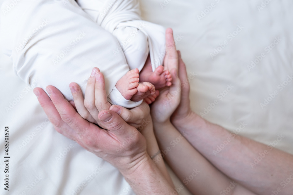 Mom and dad hands hold small legs of their two newborn twin babies Mom and dad hands hold small legs of their two newborn twin babies