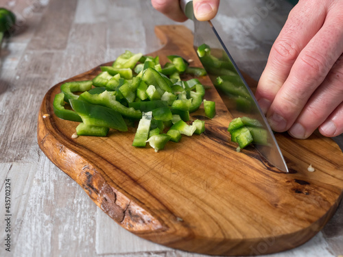Cutting green pepper with a knife on a wooden board in the kitchen, close-up photo, warm color of the photo